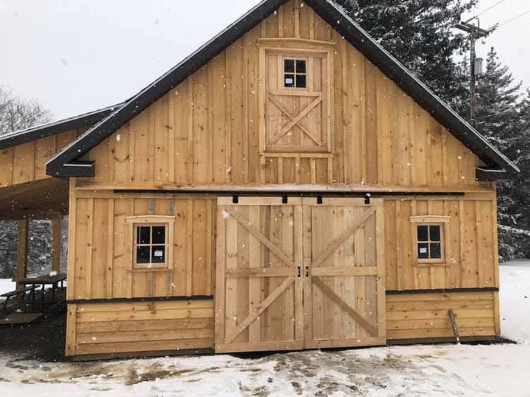 Wooden barn with snow on the ground and trees in the background